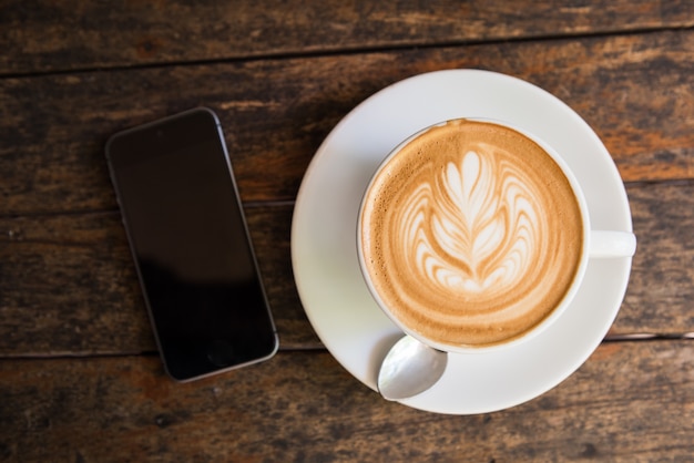 Eine Schale heißer Lattekunstkaffee mit intelligentem Telefon auf Holztisch