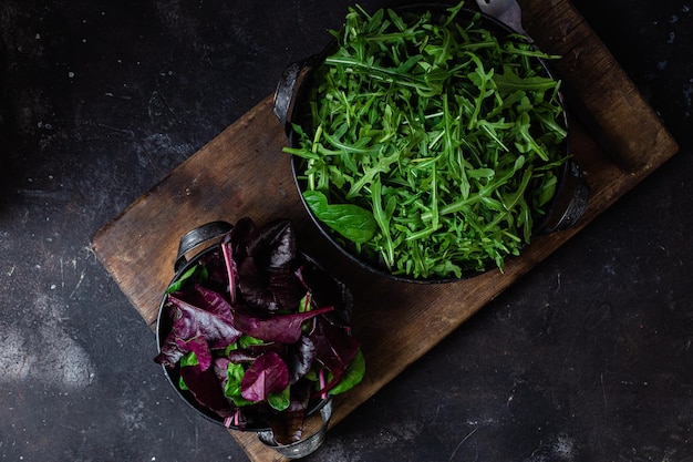 Eine Schale mit grünem Rucola steht auf einem Holzschneidebrett neben einer Schale mit grünem Rucola.