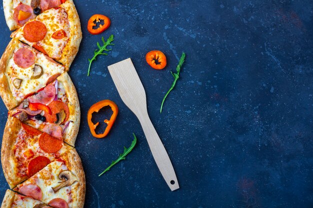 Eine Scheibe frisch zubereitete Pizza mit Salami, Pilzen, Schinken und Käse auf einem dunklen Hintergrund. Italienisches traditionelles Mittag- oder Abendessen. Fast Food und Street Food Konzept. Flache Lage,