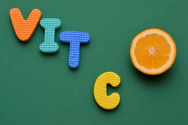 Eine Scheibe frischer Orange und Buchstaben Inschrift Vitamin C auf grünem Hintergrund