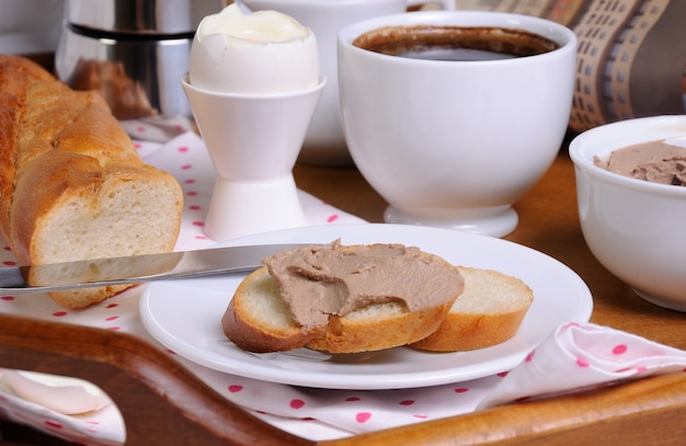 Eine Scheibe Toastbrot mit Leberpastete zum Frühstück und eine Tasse Kaffee auf einem Tablett