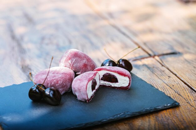 Foto eine schieferplatte mit rosa mochi und kirschen auf einem holztischmochi asiatisches dessert