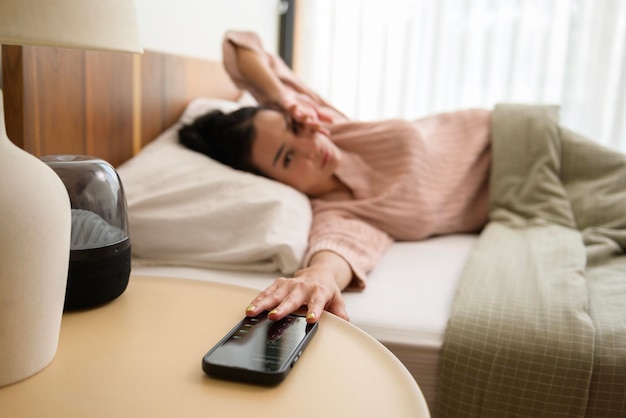 Eine schlafende asiatische Frau schaltet den Alarm auf dem Smartphone aus, während sie morgens aufgewacht wird