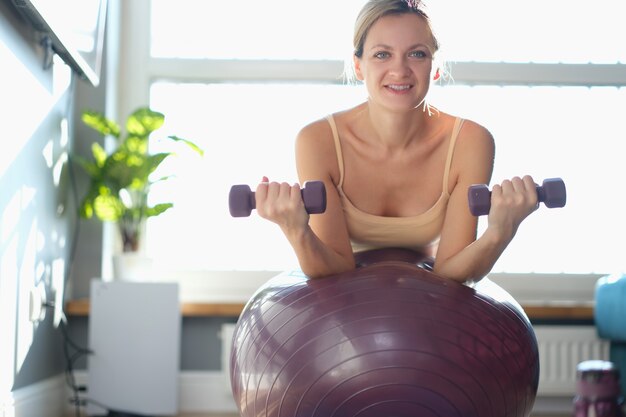 Eine schlanke Frau auf einem Sportball macht Übungen mit Hanteln