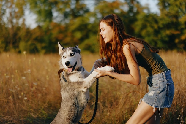 Eine schlanke Frau spielt und tanzt mit einem Husky-Hund in der Natur im Herbst auf einem Grasfeld und lächelt an einem guten Abend in der untergehenden Sonne Hochqualitätsfoto