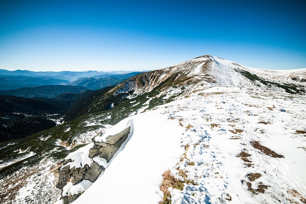 Eine schneebedeckte Bergspitze mit einem blauen Himmel und einem Berg im Hintergrund.