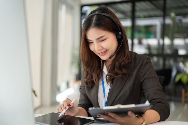 Eine schöne asiatische Call-Center-Betreiberin mit drahtlosem Headset benutzt ihr Tablet