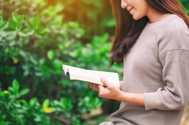 Eine schöne asiatische Frau, die ein Buch liest, während sie im Park sitzt