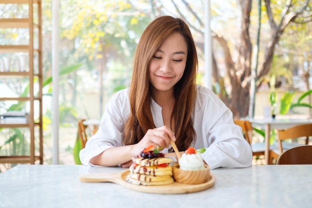 Eine schöne asiatische Frau, die Eis mit gemischten Beerenpfannkuchen und Schlagsahne mit einem Holzlöffel isst