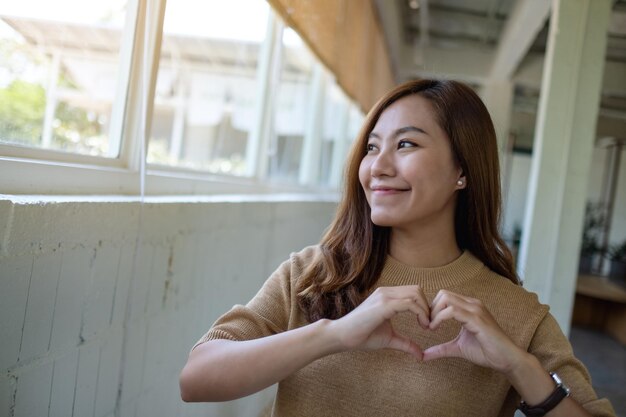 Eine schöne asiatische Frau, die Herzhandzeichen mit glücklichem Gefühl macht