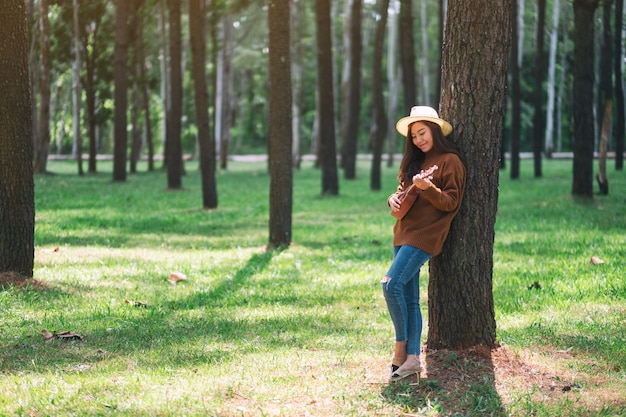 Eine schöne asiatische frau, die im park ukulele steht und spielt