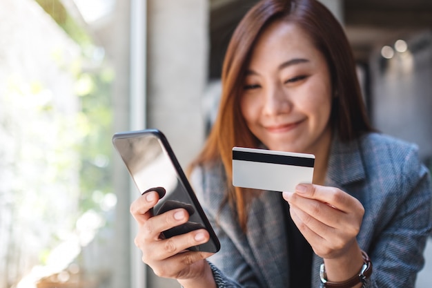 Eine schöne asiatische Frau, die Kreditkarte für Kauf und Einkauf online auf Handy verwendet