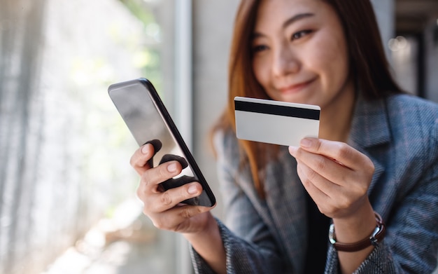 Eine schöne asiatische Frau, die Kreditkarte für Kauf und Einkauf online auf Handy verwendet
