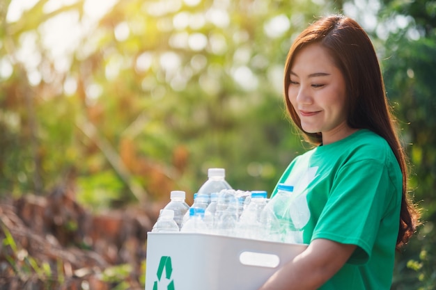 Eine schöne asiatische Frau, die Müll sammelt und einen Papierkorb mit Plastikflaschen im Freien hält