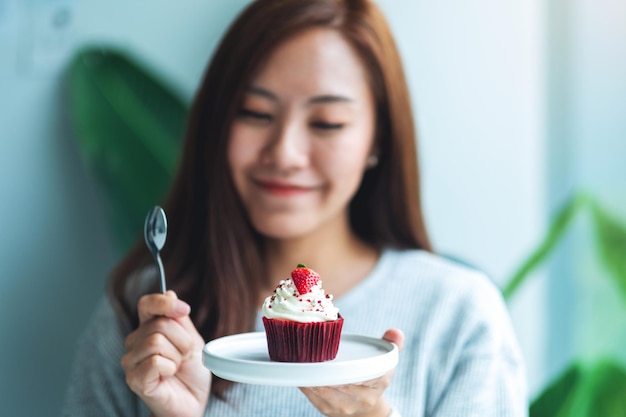 Eine schöne asiatische Frau, die roten Samtschalenkuchen hält und isst