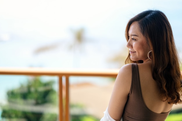 Eine schöne asiatische Frau, die steht und genießt, den Meerblick auf Balkon zu beobachten