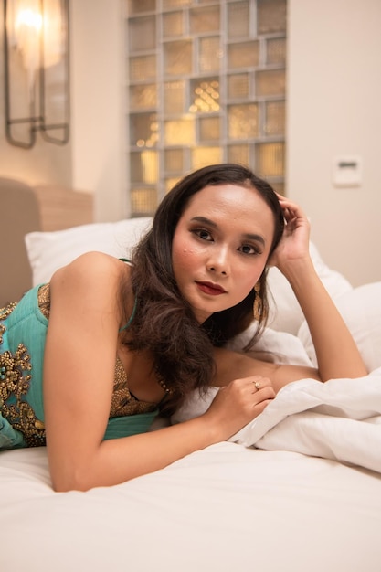 Eine schöne asiatische Frau entspannt sich nachmittags auf einem weißen Bett, während sie Make-up trägt und sich anzieht
