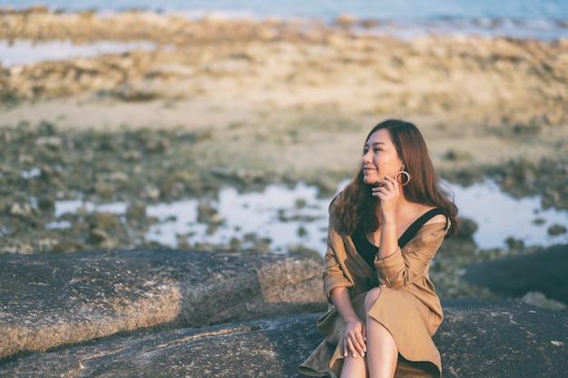 Eine schöne asiatische Frau genießt es, auf dem Felsen an der Küste zu sitzen