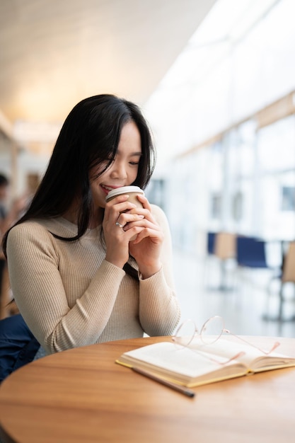 Eine schöne asiatische Frau genießt ihren Kaffee, während sie fern in einem Café arbeitet