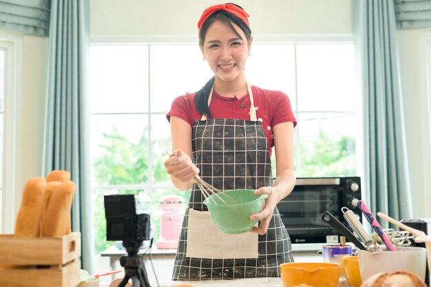 Eine schöne asiatische Frau macht Bäckerei, Live-Streaming oder nimmt Videos in sozialen Medien in ihrem Haus auf