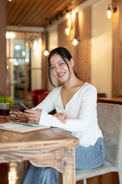 Eine schöne asiatische Frau sitzt mit einem Smartphone in der Hand an einem Tisch in einem schönen Café