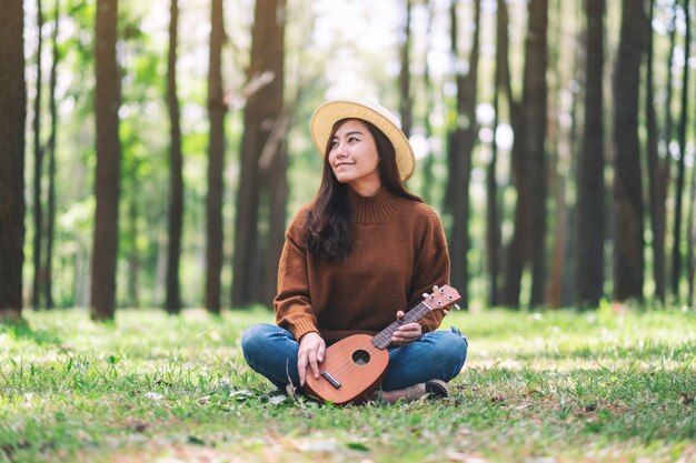 Eine schöne asiatische Frau sitzt und spielt Ukulele im Park