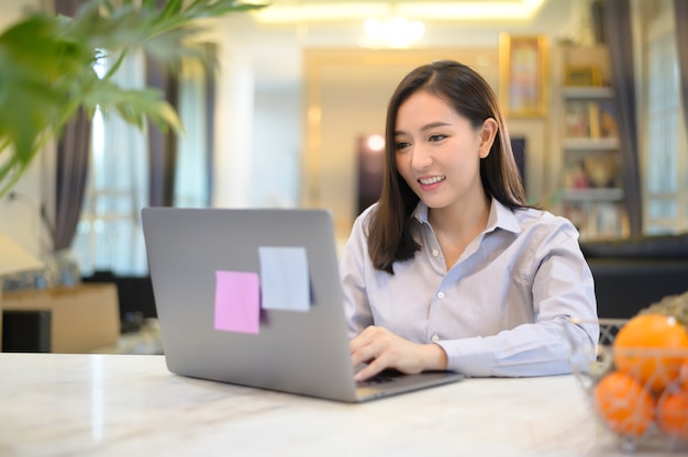 Eine schöne asiatische Geschäftsfrau arbeitet zu Hause mit ihrem Computer.