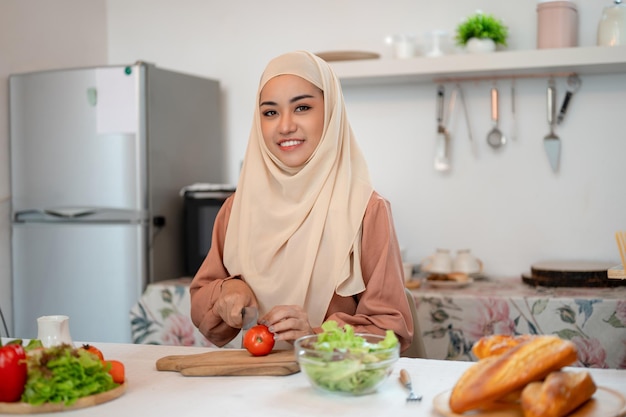 Eine schöne asiatische muslimische Frau bereitet in einer Küche Zutaten für ihre gesunde Salatmischung vor