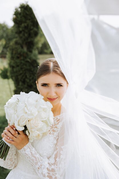 Eine schöne Braut in einem unglaublich schönen Kleid genießt einen Blumenstrauß und schnuppt ihn Sommerhochzeit eine luxuriöse Braut