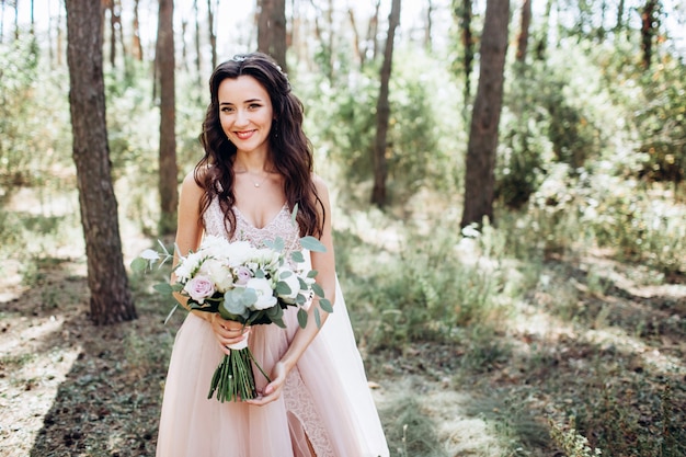 Eine schöne Braut in einem zarten rosa Kleid im Freien, Das Mädchen hält einen Blumenstrauß