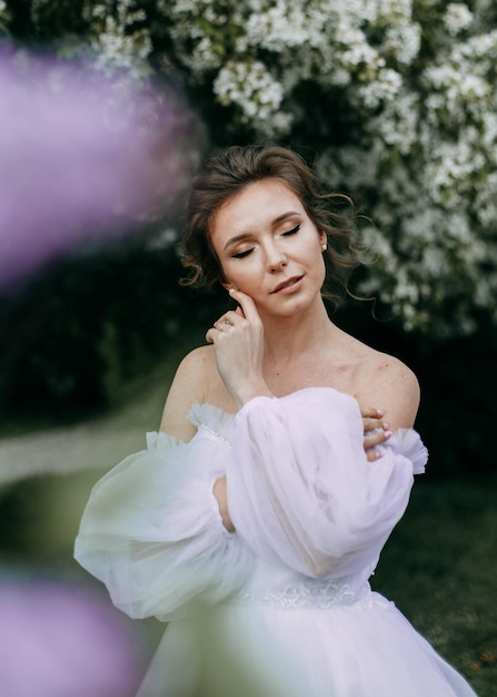 Eine schöne, delikate, elegante Frau, Braut in einem Hochzeitskleid, geht alleine in einem Frühlingspark im Freien