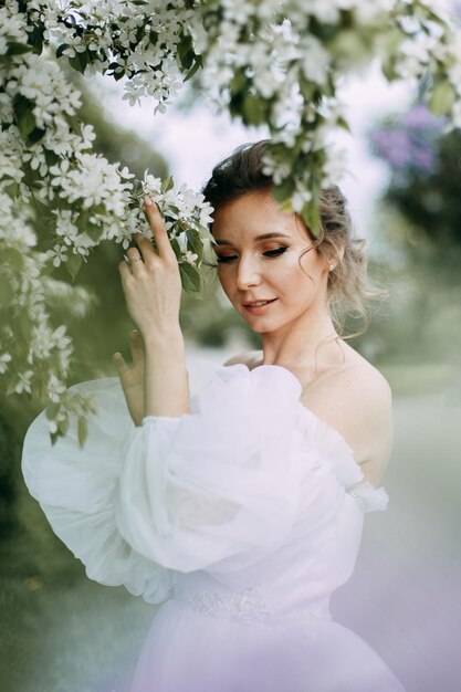 Eine schöne, delikate, elegante Frau, Braut in einem Hochzeitskleid, geht alleine in einem Frühlingspark im Freien