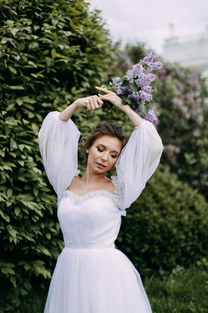 Eine schöne, delikate, elegante junge Braut in einem Hochzeitskleid geht allein in einem blühenden Park spazieren.