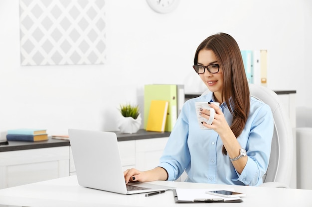 Eine schöne, erfolgreiche Frau mit einer Tasse Kaffee, die im modernen Büro arbeitet