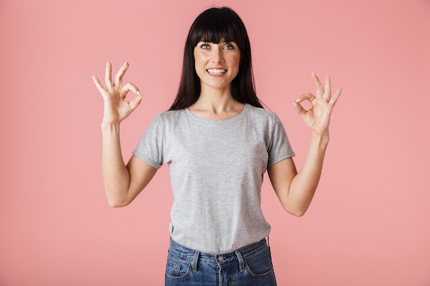 eine schöne erstaunliche frau, die isoliert über hellrosa wand posiert und eine ok geste zeigt.