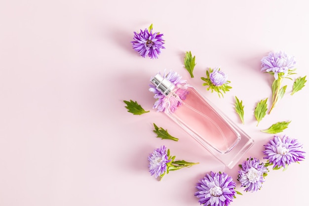 Eine schöne Flasche Damenparfüm oder Kosmetikspray auf rosafarbenem Hintergrund zwischen Herbstblumen ein Kopierraum Eine leere Layout-Aromapräsentation