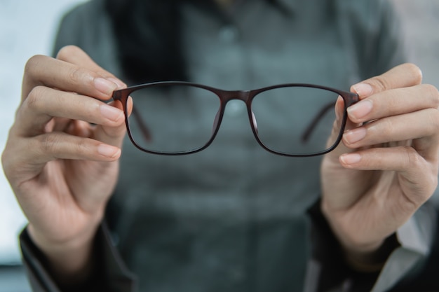 Eine schöne Frau, die eine Probe der Brille in einer Augenklinik gegen einen Brillenanzeigefensterhintergrund hält