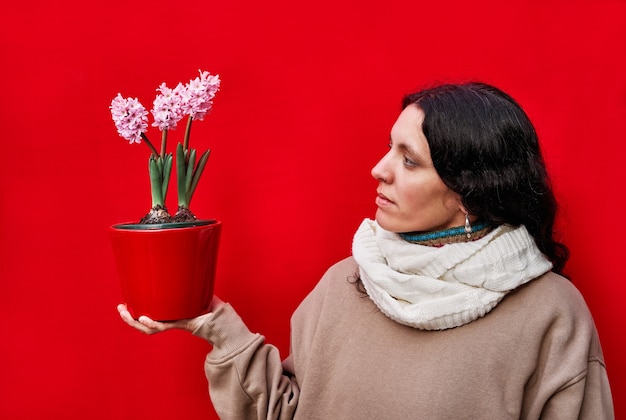 Eine schöne Frau, die einen Topf mit Hyazinthenpflanzen auf roter Wand hält