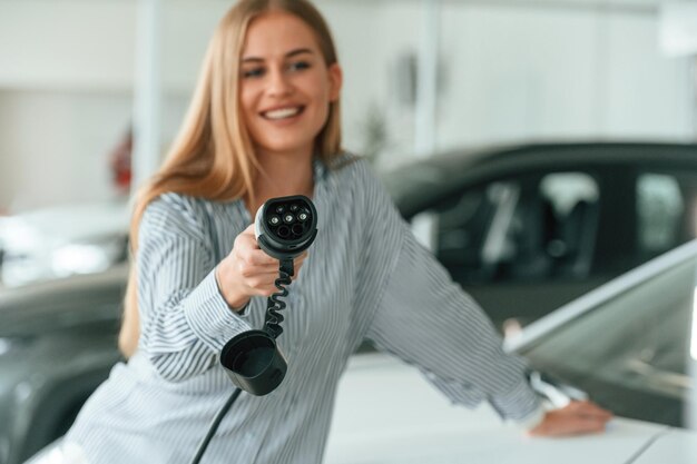 Foto eine schöne frau hält ein ladegerät für ein elektroauto im haus.