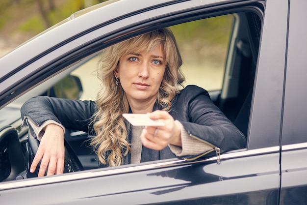 Eine schöne Frau im Autofenster zeigt einen Führerschein