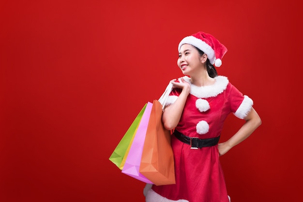 Eine schöne Frau im Weihnachtsmannkostüm, das Einkaufstaschen anlässlich der frohen Weihnachten und des guten Rutsch ins Neue Jahr hält.