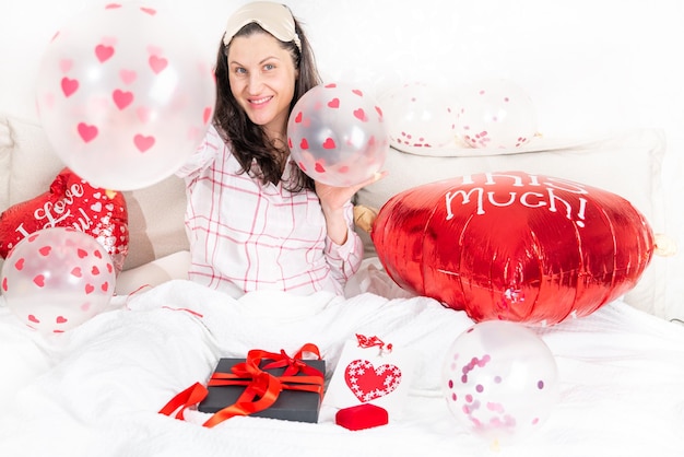 Eine schöne Frau in rosa Schlafanzug mit einem herzförmigen Ballon liegt zu Hause auf dem Bett