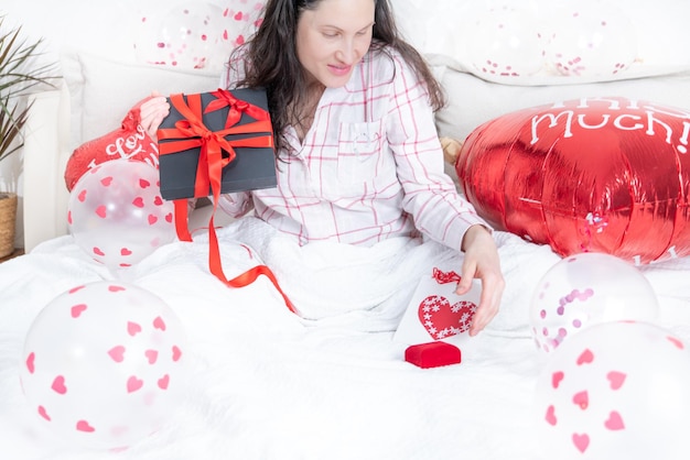 Eine schöne Frau in rosa Schlafanzug mit einem herzförmigen Ballon liegt zu Hause auf dem Bett