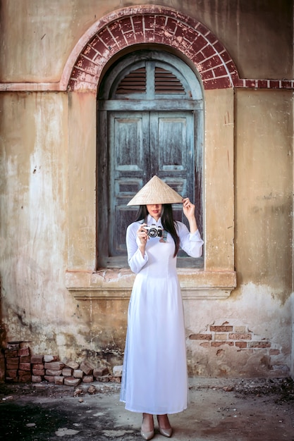 Foto eine schöne frau in vietnams nationaltracht steht und fängt einen sonnenhut. beim fotografieren