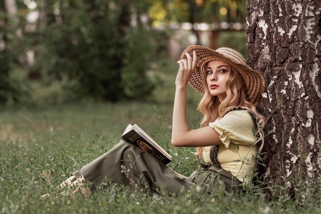 Eine schöne Frau mit blonden Haaren im Park oder Garten, die ein Buch liest