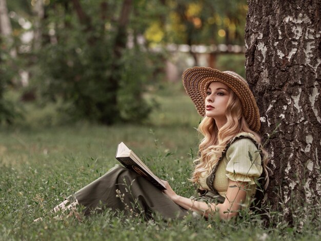 Eine schöne Frau mit blonden Haaren im Park oder Garten, die ein Buch liest