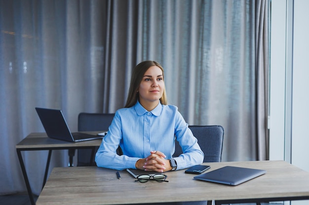 Eine schöne Frau mit Brille sitzt an einem Tisch im Büro und arbeitet an einem Laptop Unternehmensarbeit im Büro Moderne Arbeitsplatzleiterin in klassischer Kleidung