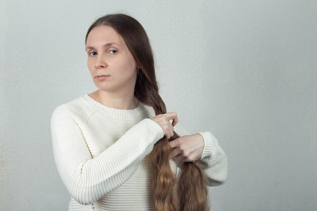 Eine schöne Frau mit langen Haaren zöpft einen Zopf auf einem weißen strukturierten Hintergrund