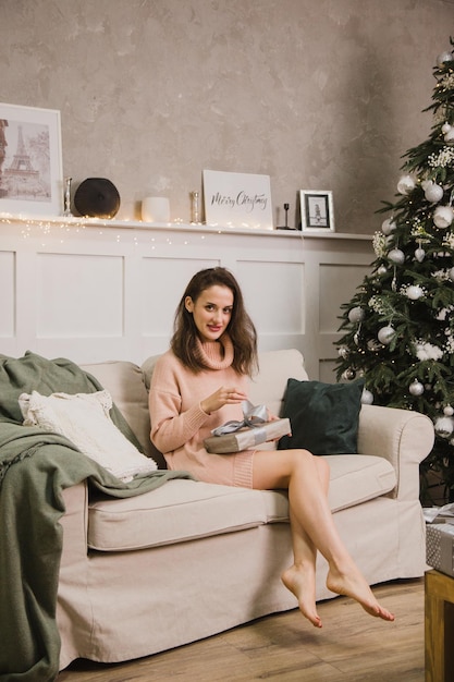 Eine schöne Frau sitzt auf dem Sofa neben dem Weihnachtsbaum und liest ein Buch. Silvester und Weihnachten