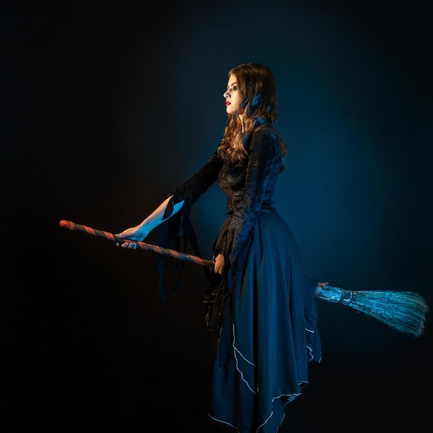 Eine schöne Hexe auf einem Besenstiel fliegt zum Sabbat, eine junge brünette Frau in einem Kleid und mit